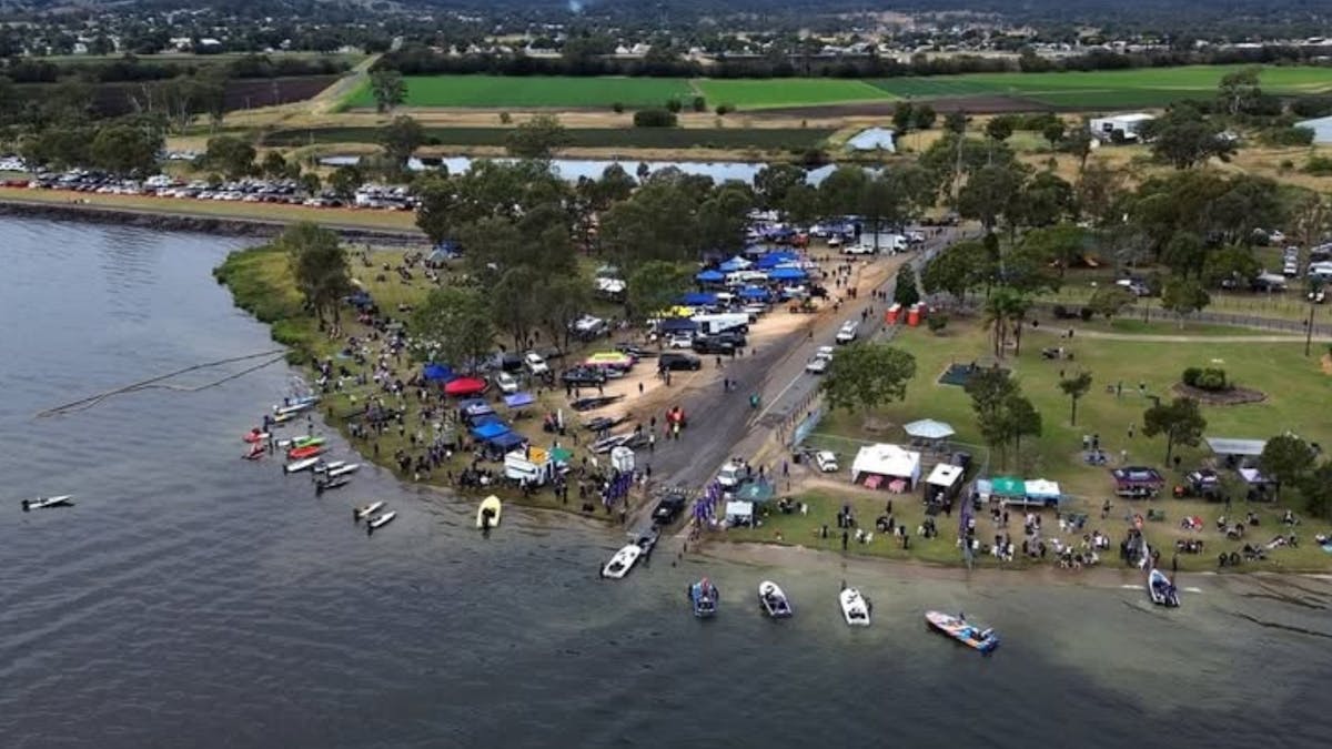 Drone shot looking over lake back to land where marquees, boats and crowds fill the scene