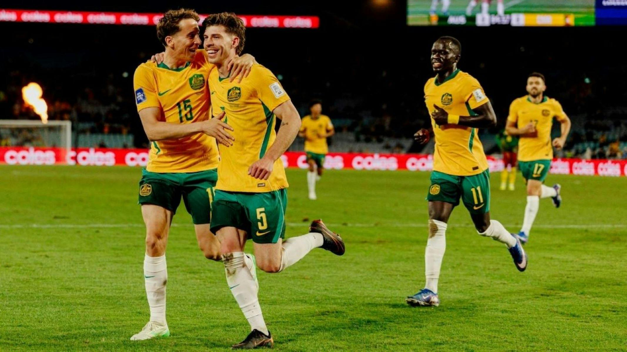 Soccer players in yellow kits celebrate a goal on a stadium pitch as teammates run in behind