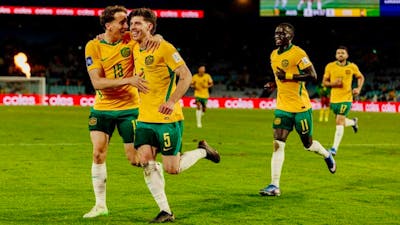 Soccer players in yellow kits celebrate a goal on a stadium pitch as teammates run in behind