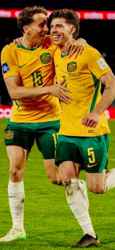 Soccer players in yellow kits celebrate a goal on a stadium pitch as teammates run in behind
