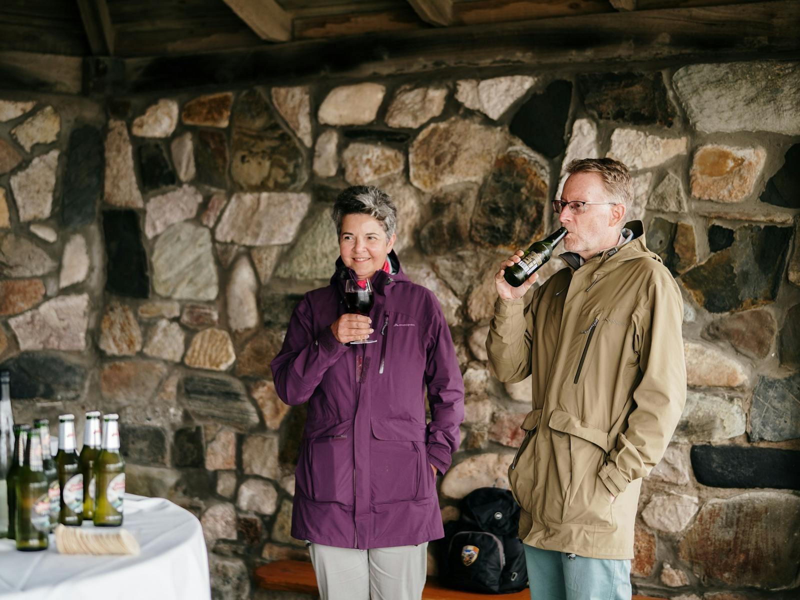 Couple smiling as they hold and drink Tasmanian alcohol beverages in stone walled picnic hut