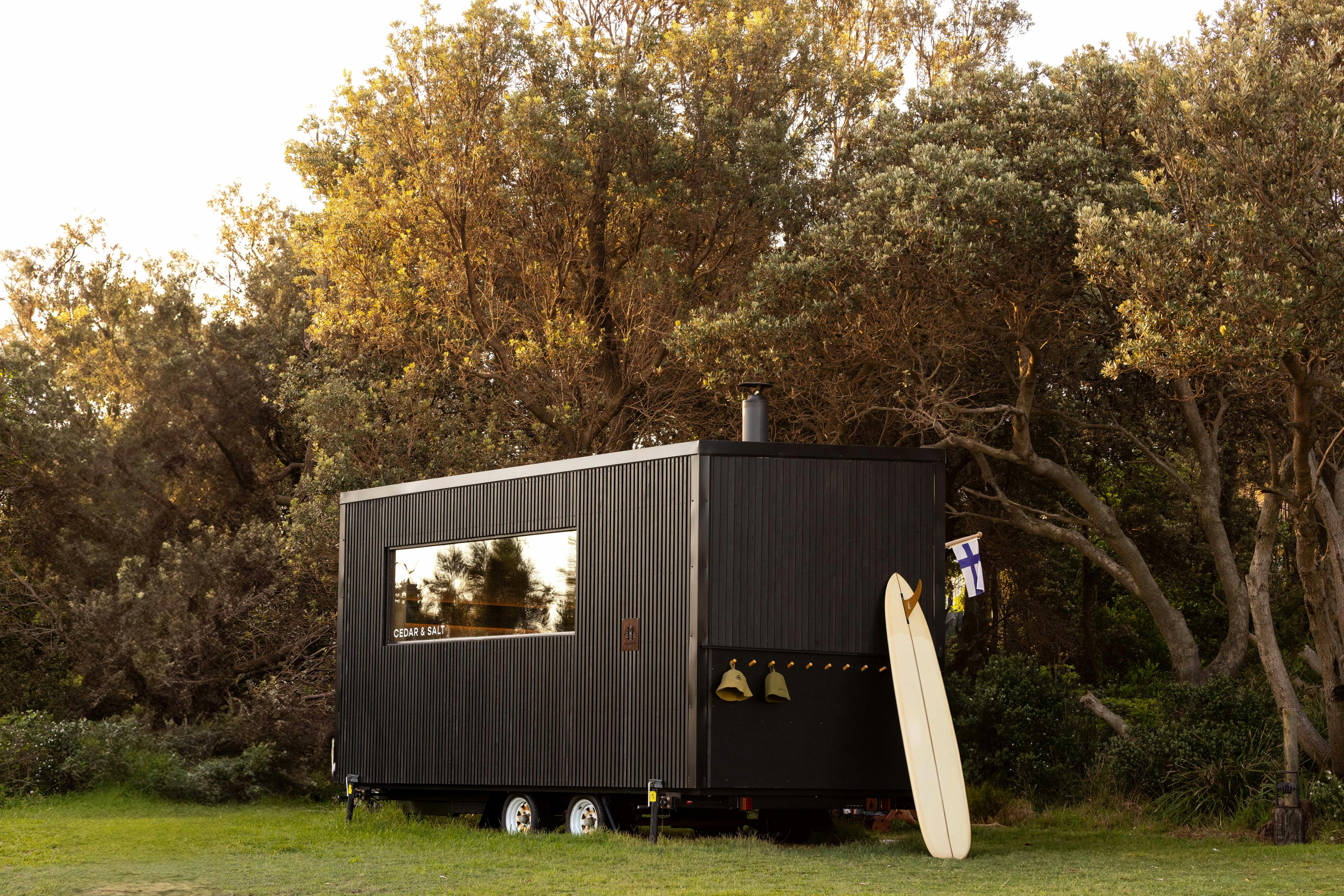 Surfboard leaning up against a mobile outdoor woodfire beachside sauna at Long Reef Beach