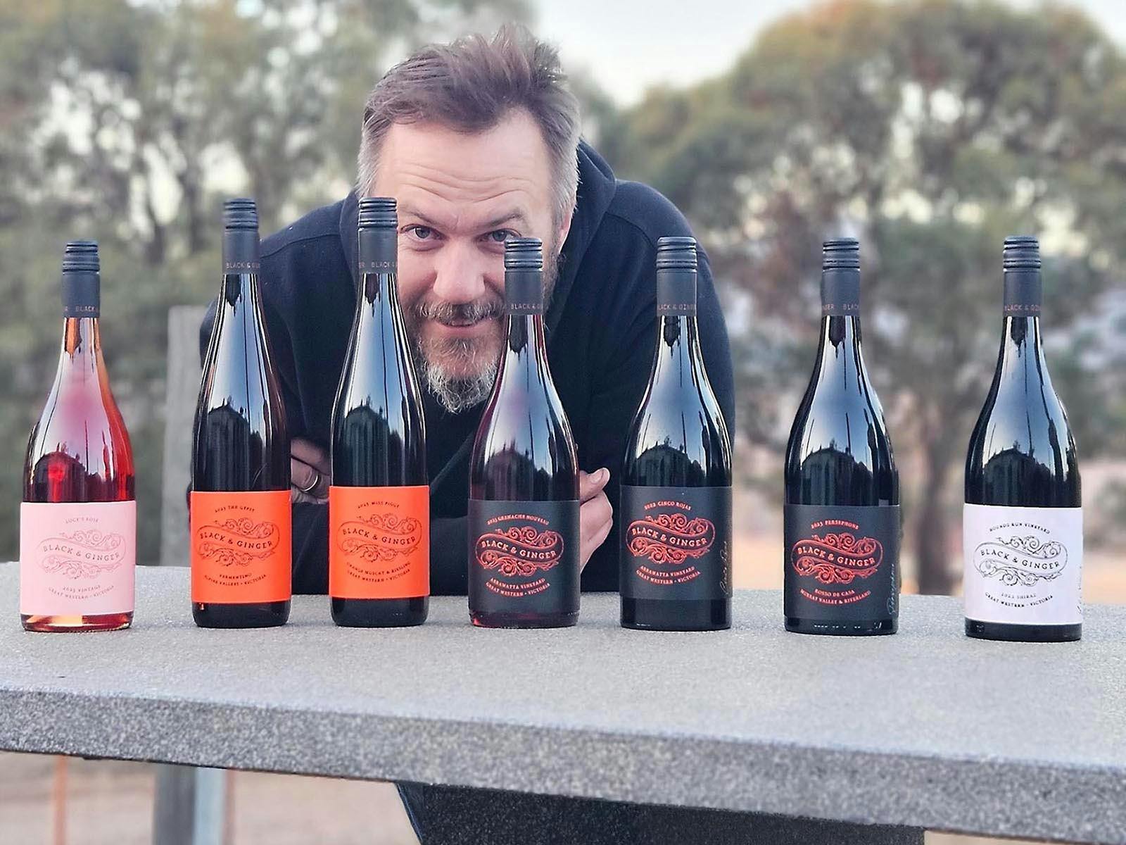 Winemaker Hadyn Black with a cheeky smile behind a line up of Black and Ginger Wines