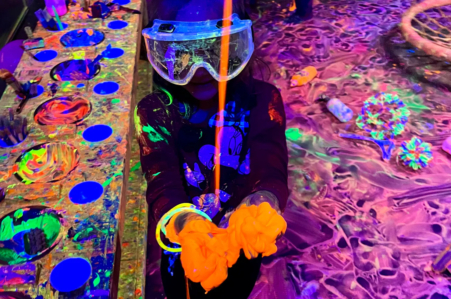 child with goggles on catching pouring glowing paint at Messy Glow Co UV Paint Room