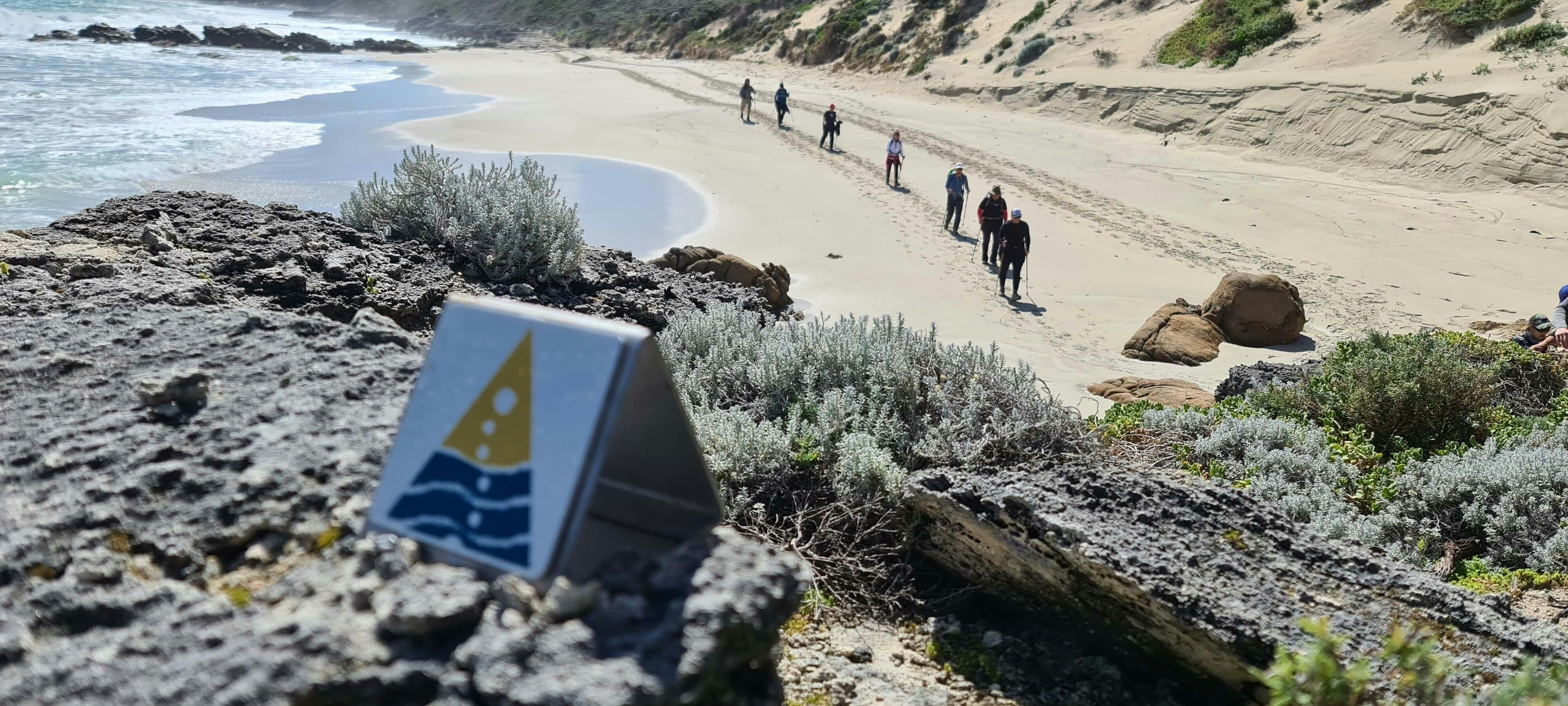 Track marker out of focus in foreground, the background is people walking in a line on the beach