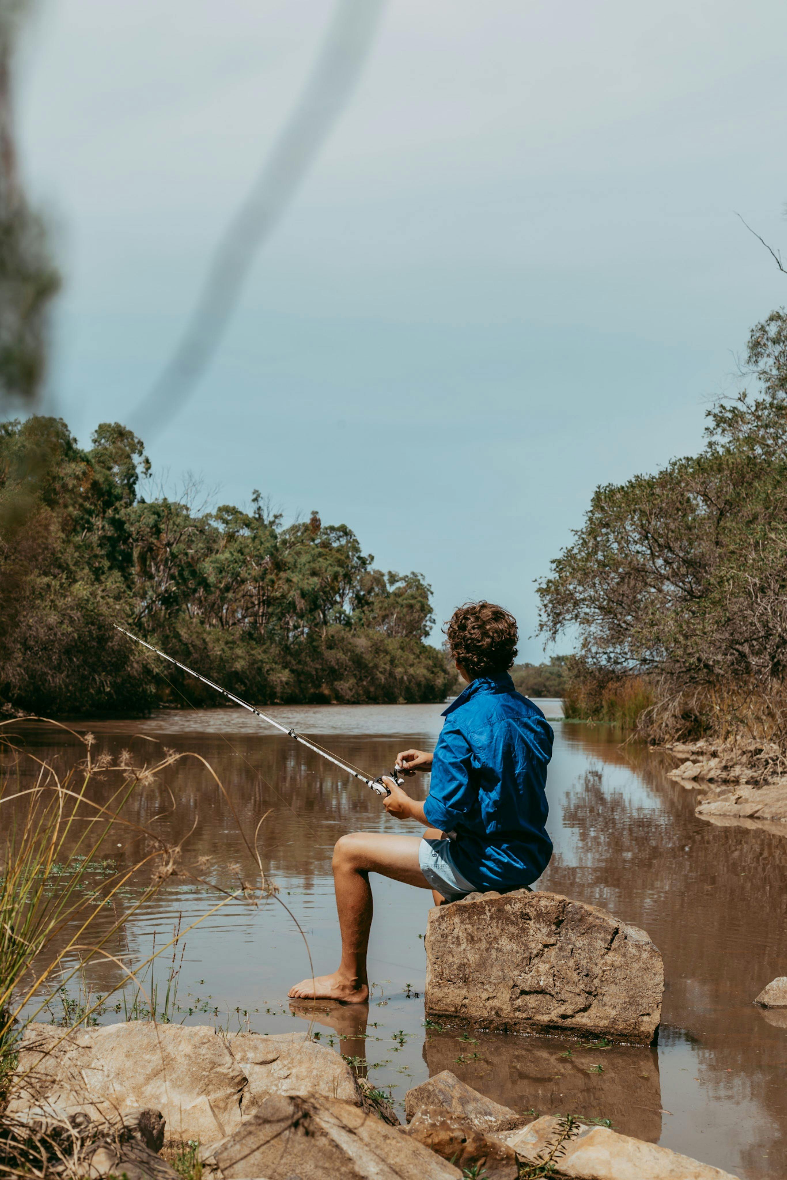 Young boy sitting on a rock fishing into a river
