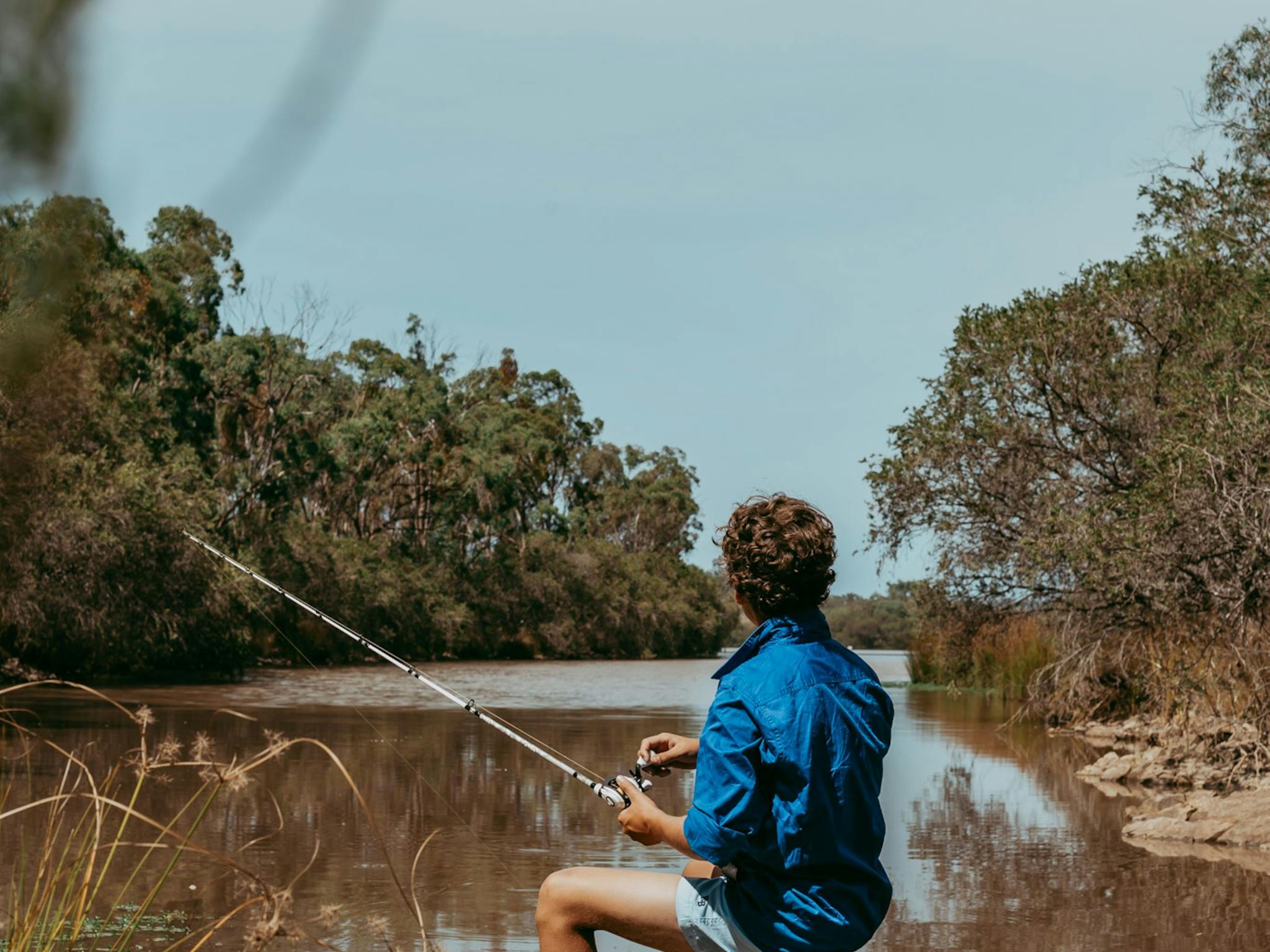 Young boy sitting on a rock fishing into a river Young boy sitting on a rock fishing into a river
