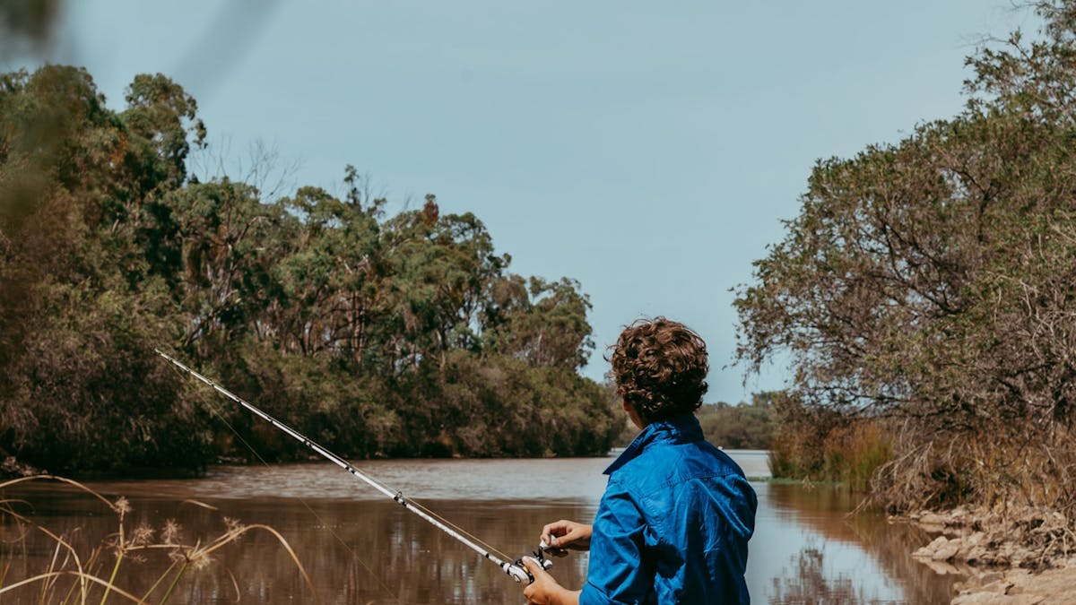 Young boy sitting on a rock fishing into a river