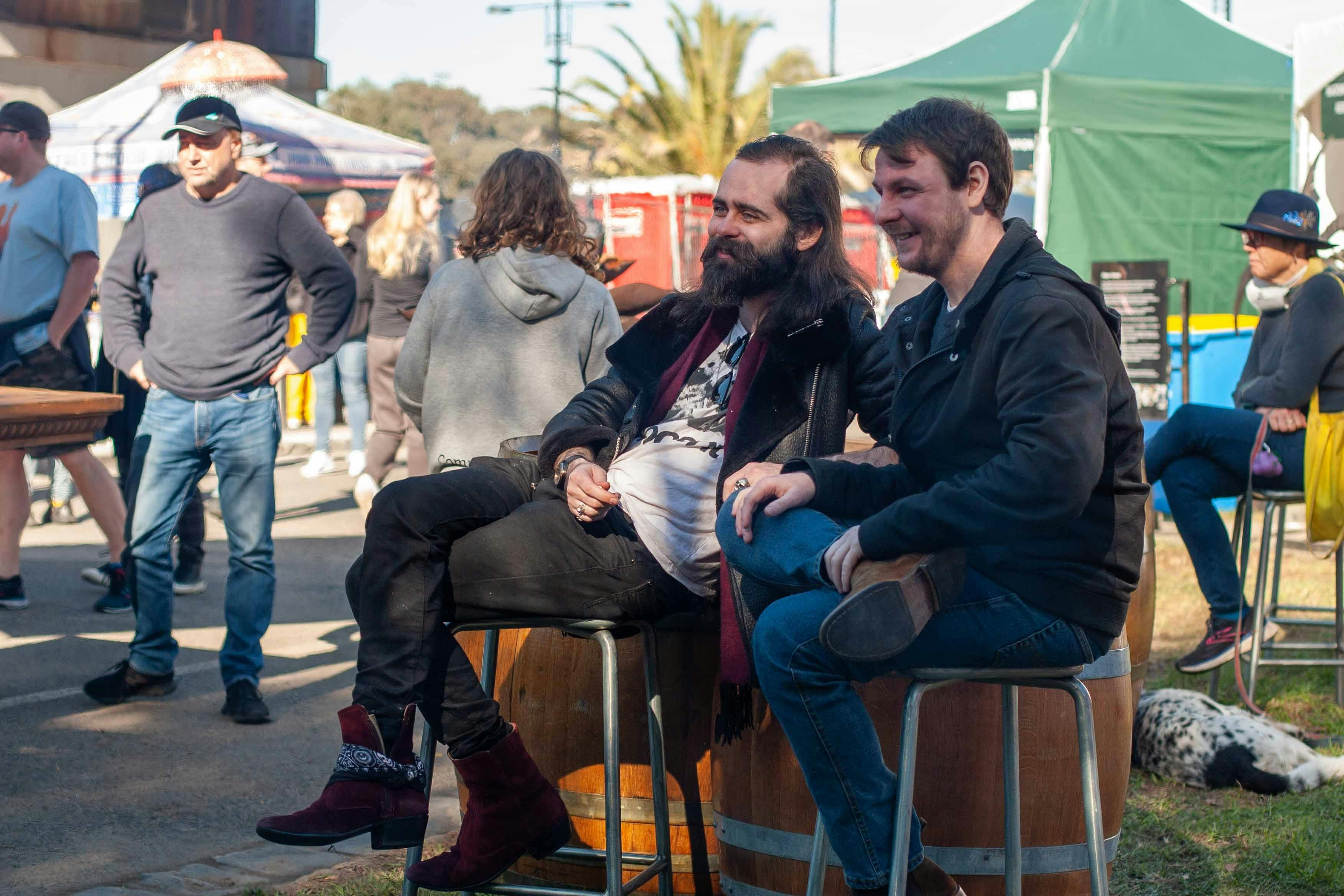 Attendees sit and talk near the festival bar while watching blacksmiths work in the background