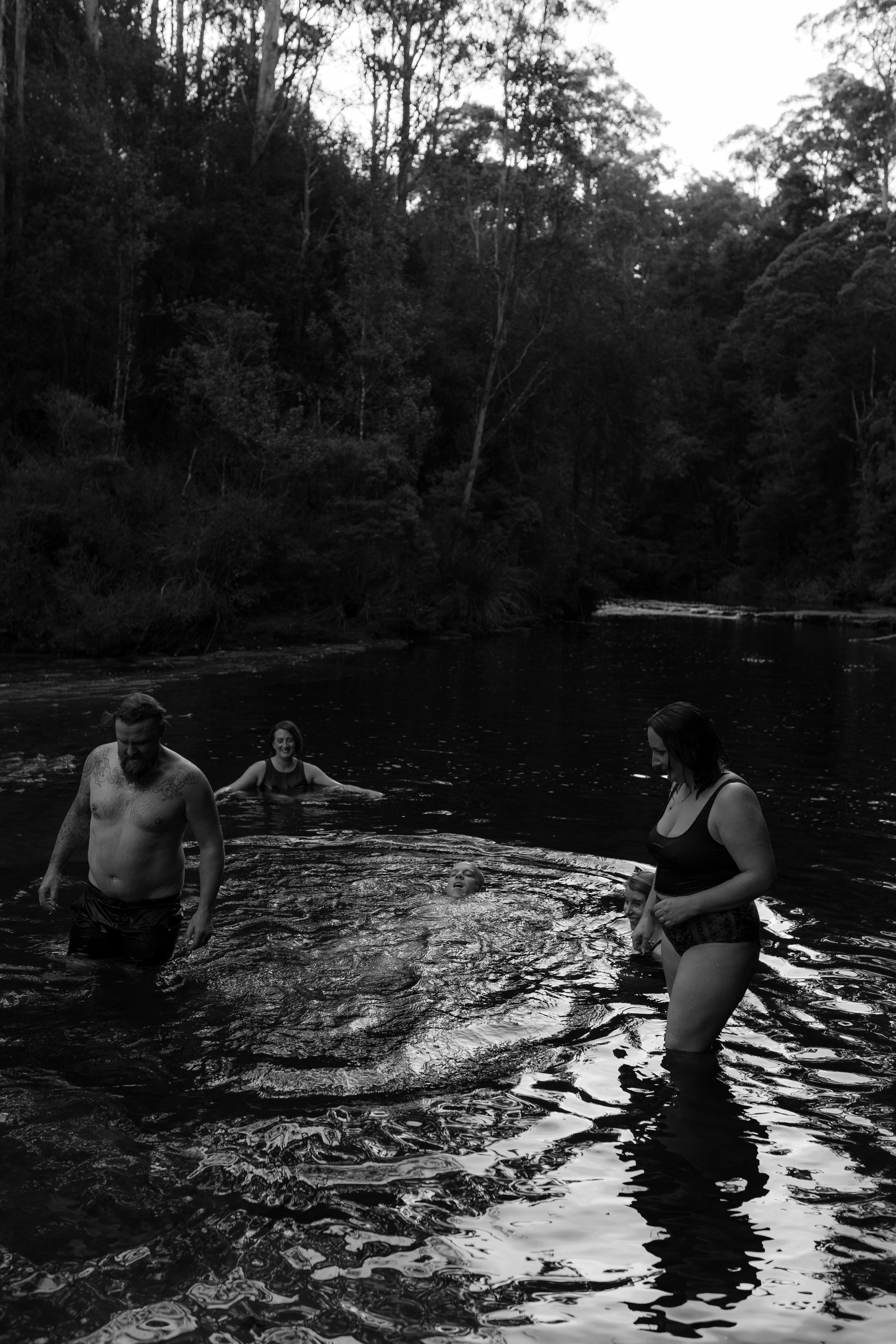 Group of guests standing in a river surrounded by native forest and bushland.