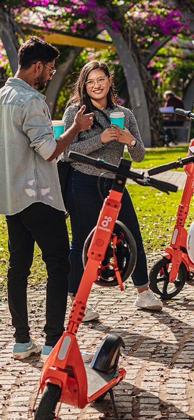 Group of people standing next to scooters on their phone