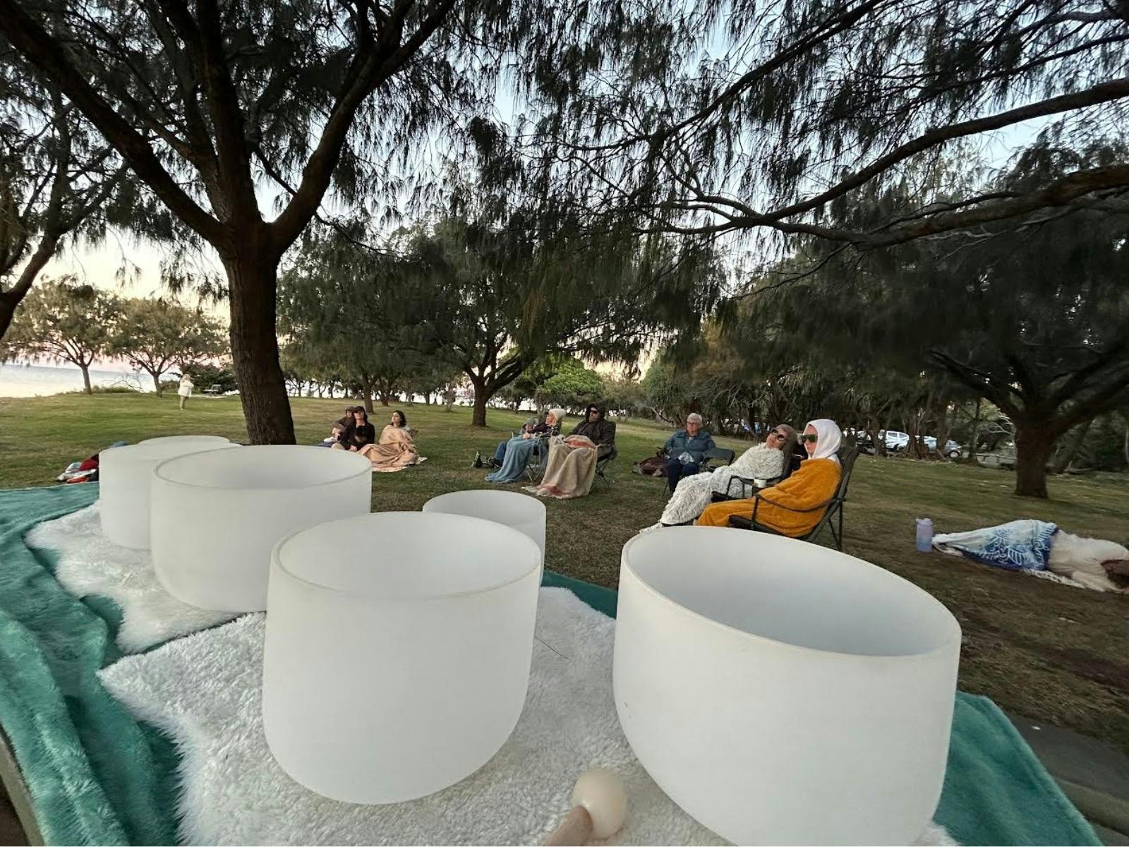 Photo of singing bowls and people sitting in the park near the ocean