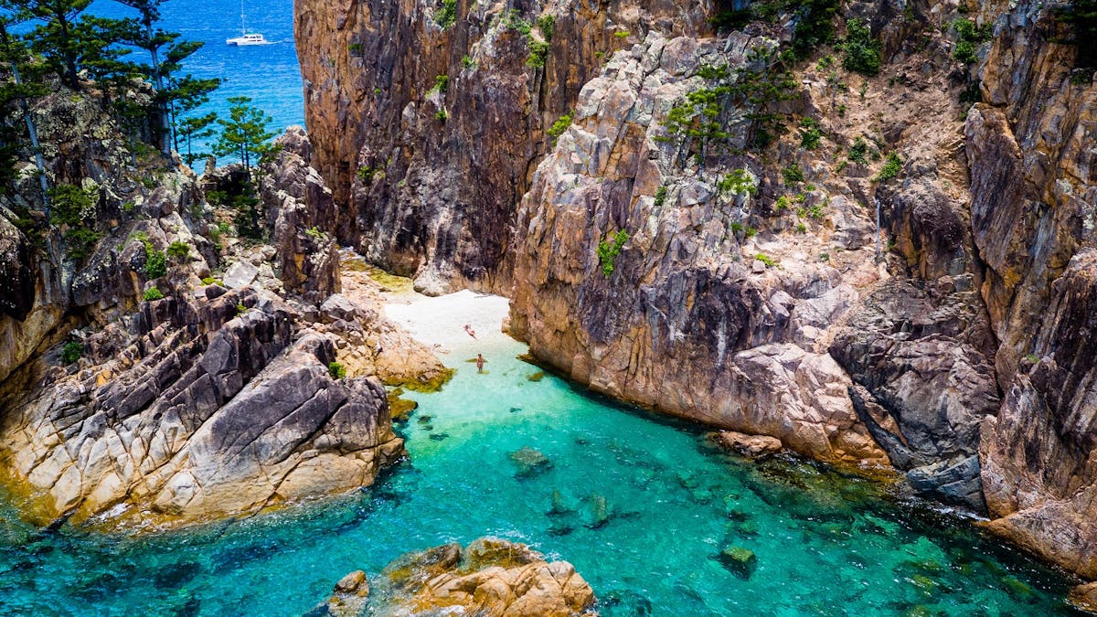 Aerial photo with a few people on the beach with rocks. coral and boat in the distance in the water