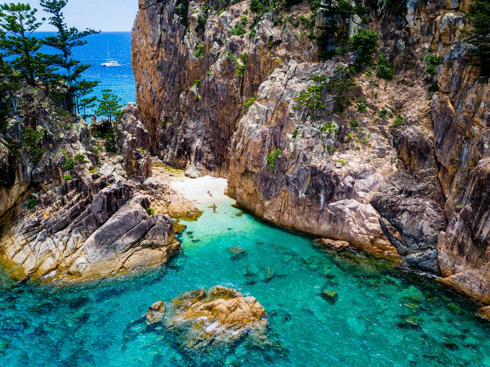 Aerial photo with a few people on the beach with rocks. coral and boat in the distance in the water Aerial photo with a few people on the beach with rocks. coral and boat in the distance in the water