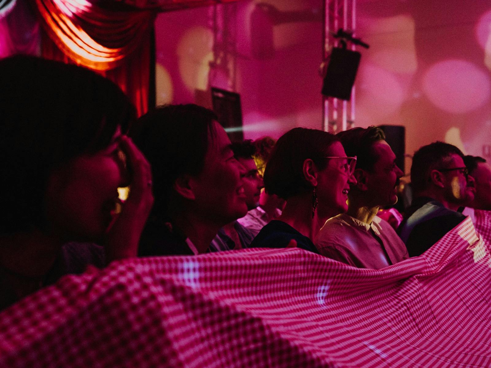 Smiling audience members shield their clothes with a gingham tablecloth.