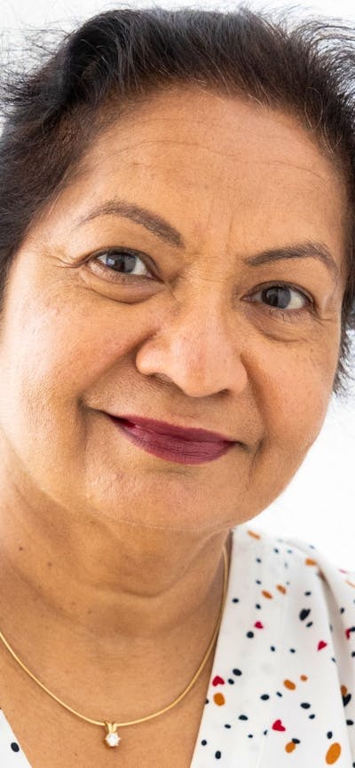 A woman smiling while resting her right hand on her left shoulder, while wearing a polka dot shirt.