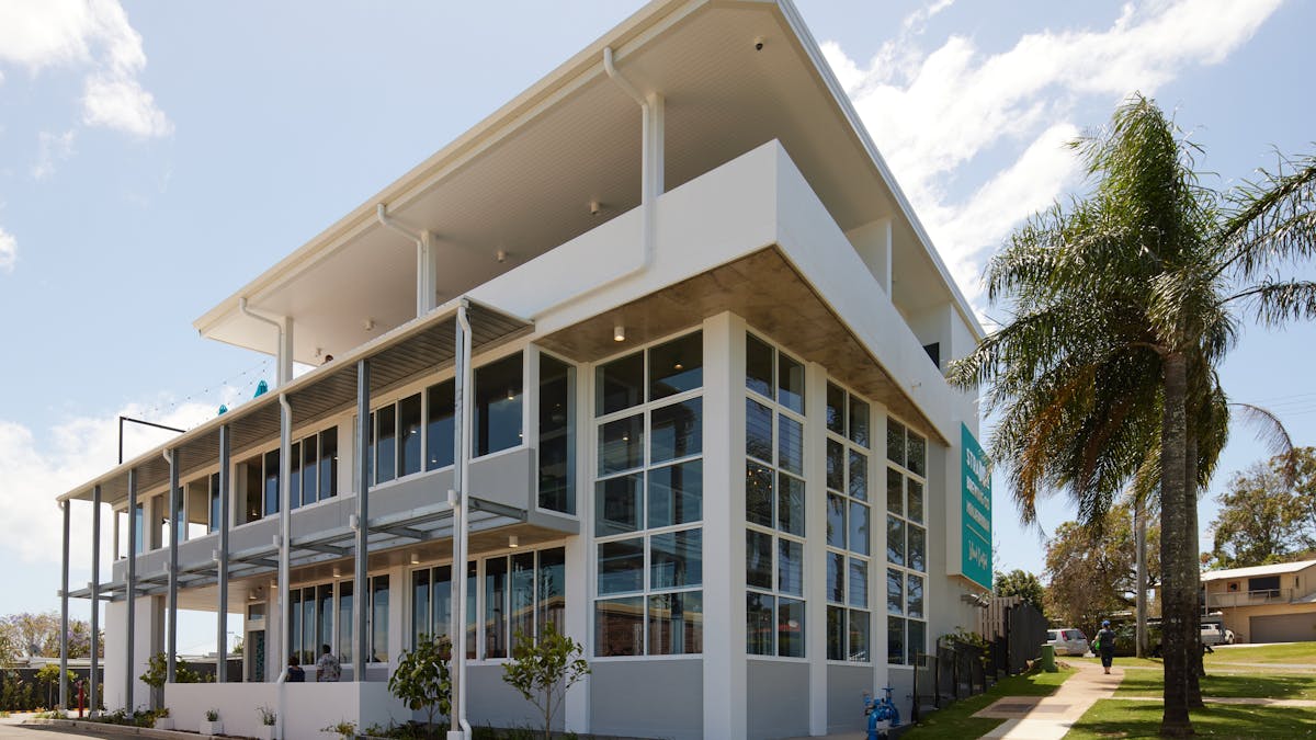 Three story white building, surrounded by palm trees