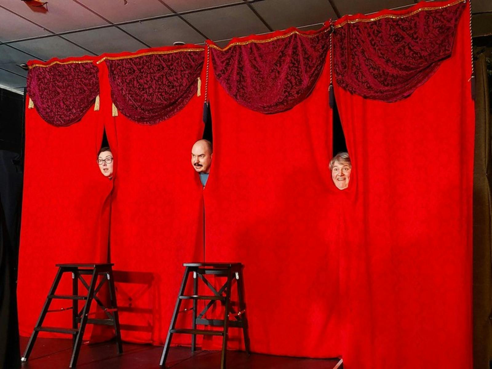 Bright red theatre curtains with three heads popping out with funny faces in three separate gaps