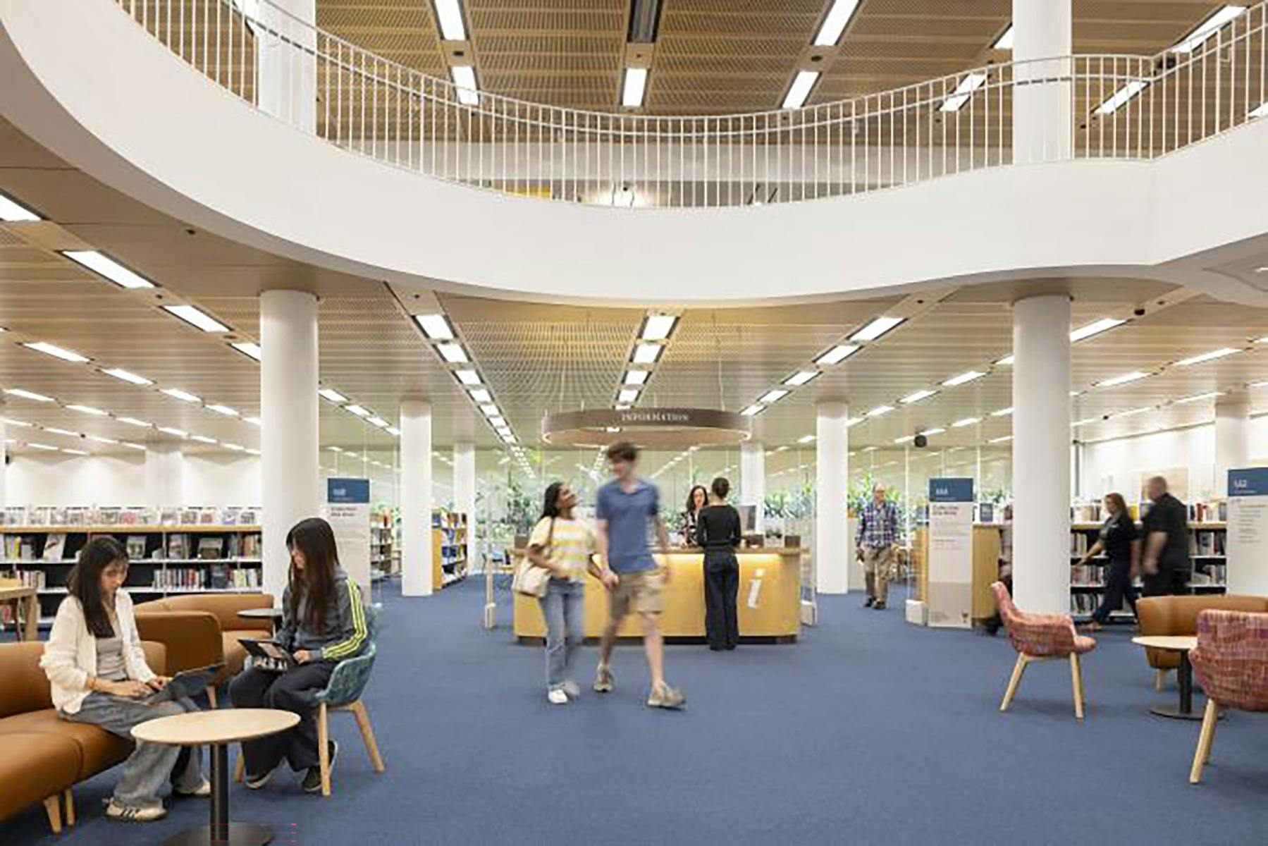 A modern library with people walking through and being served at the information desk
