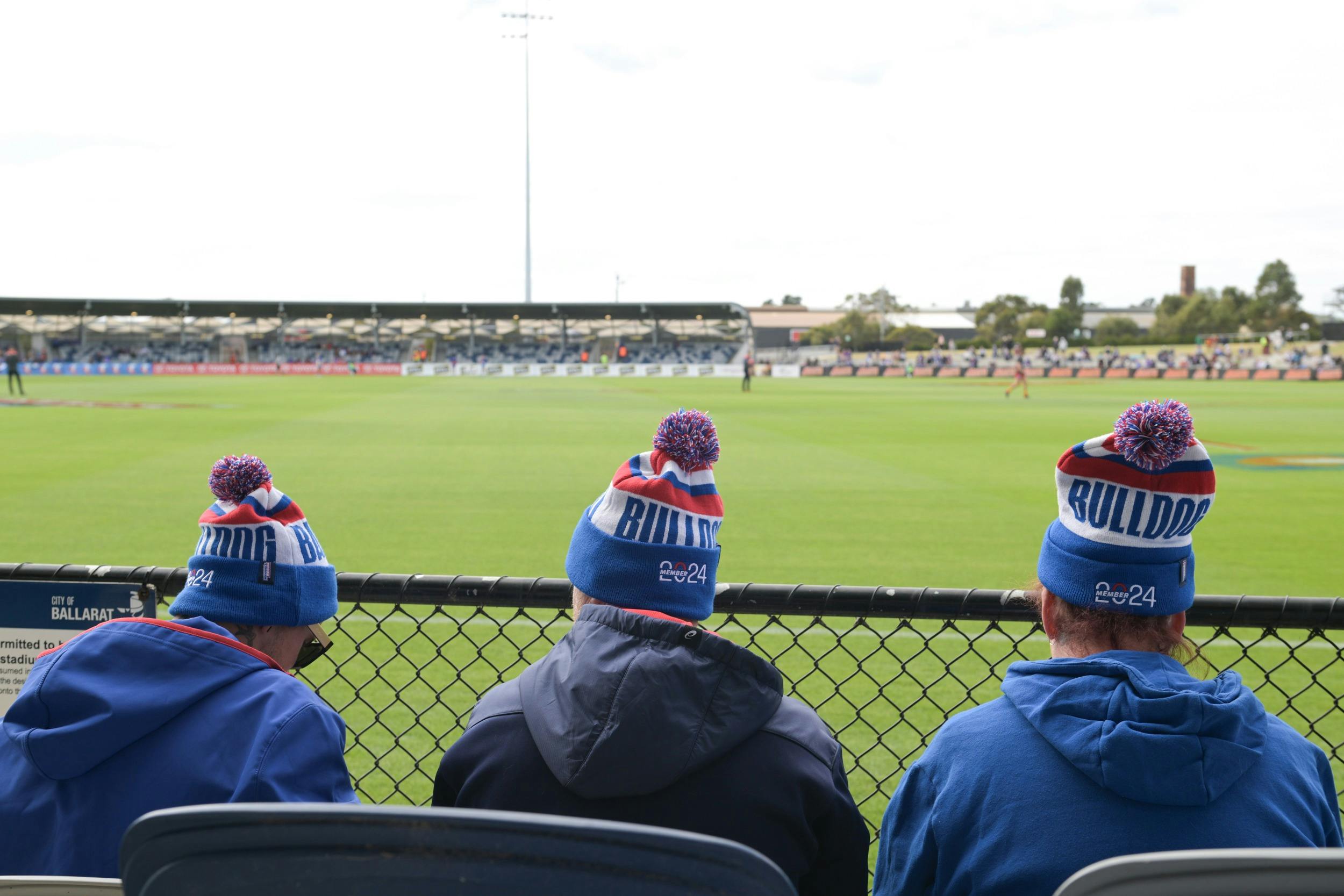 Fans sit at the fence with beanies on