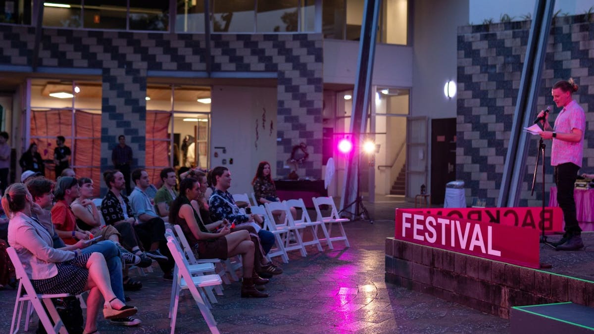 A crowd sitting on white chairs looking at a man giving a speech on stage