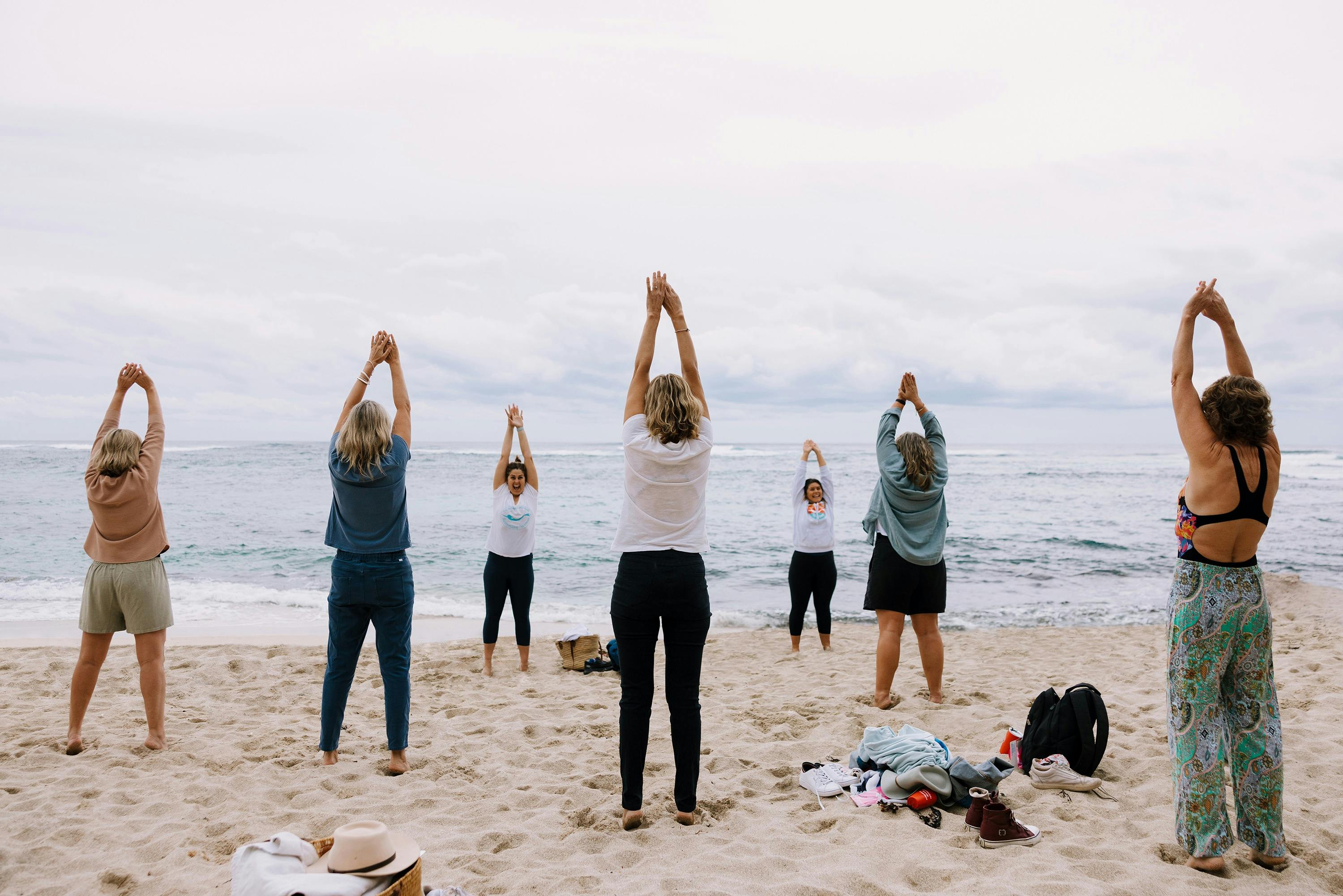 Ladies stand with their hands above their head, looking out to sea copying a guide