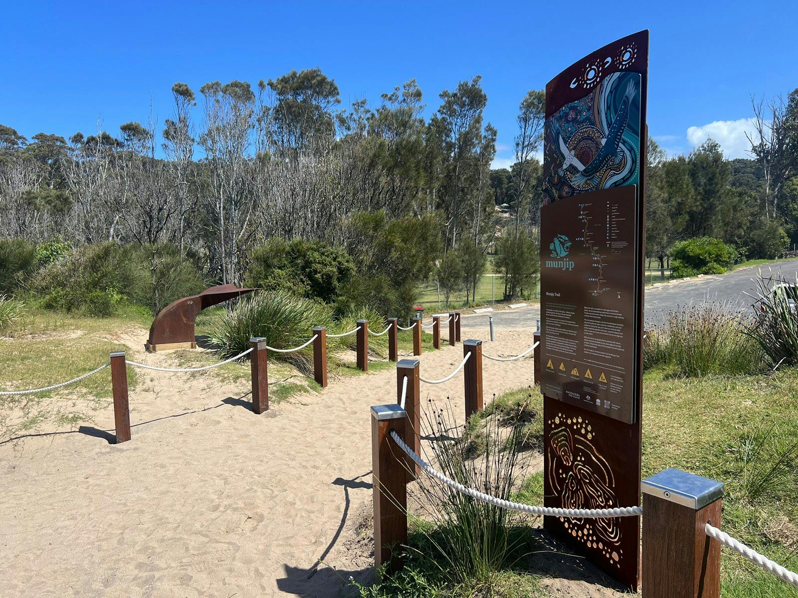 A beach track entryway with rope fencing, signage and whale tail sculpture
