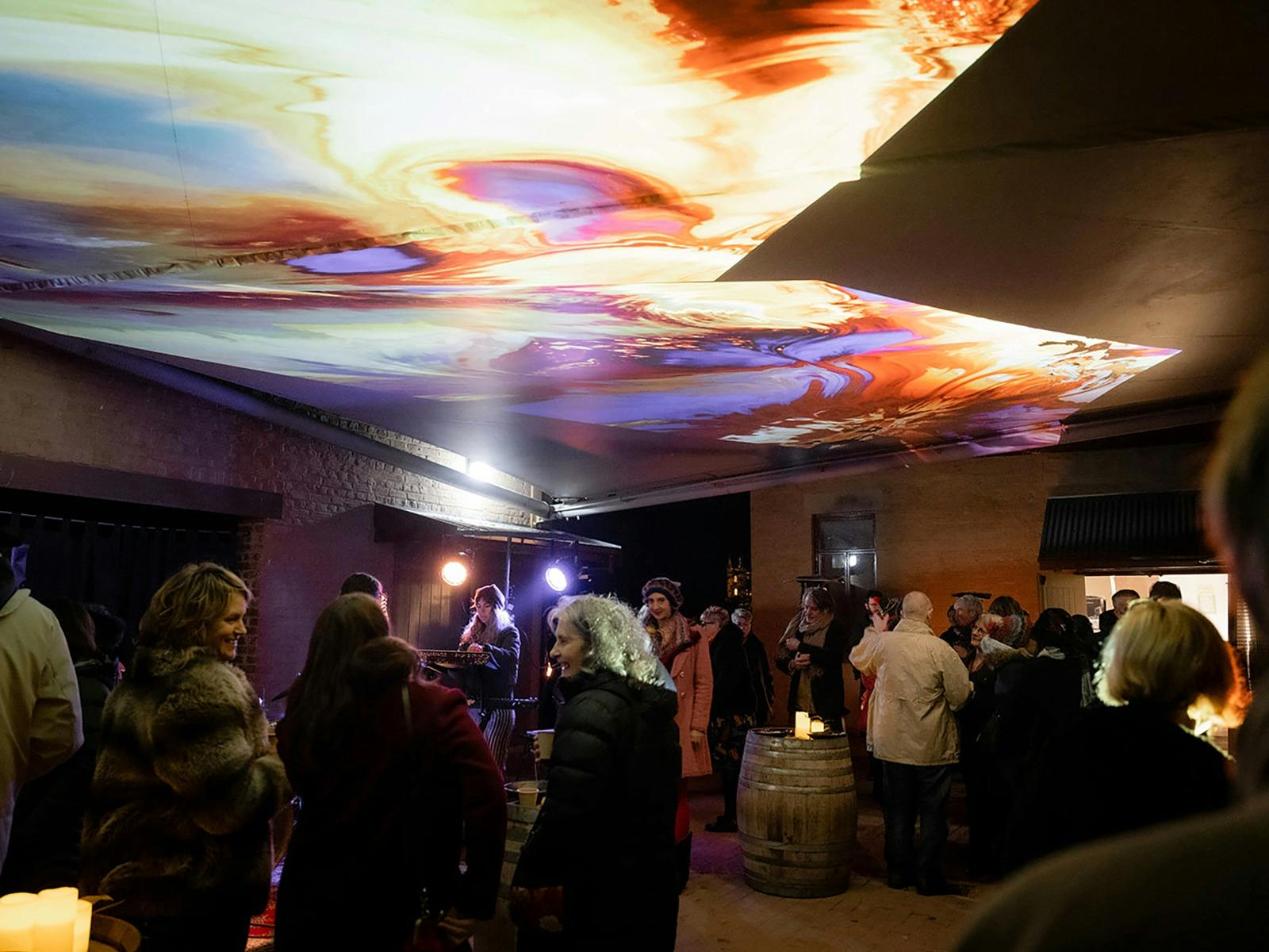 are milling in a courtyard under a brightly coloured projection.