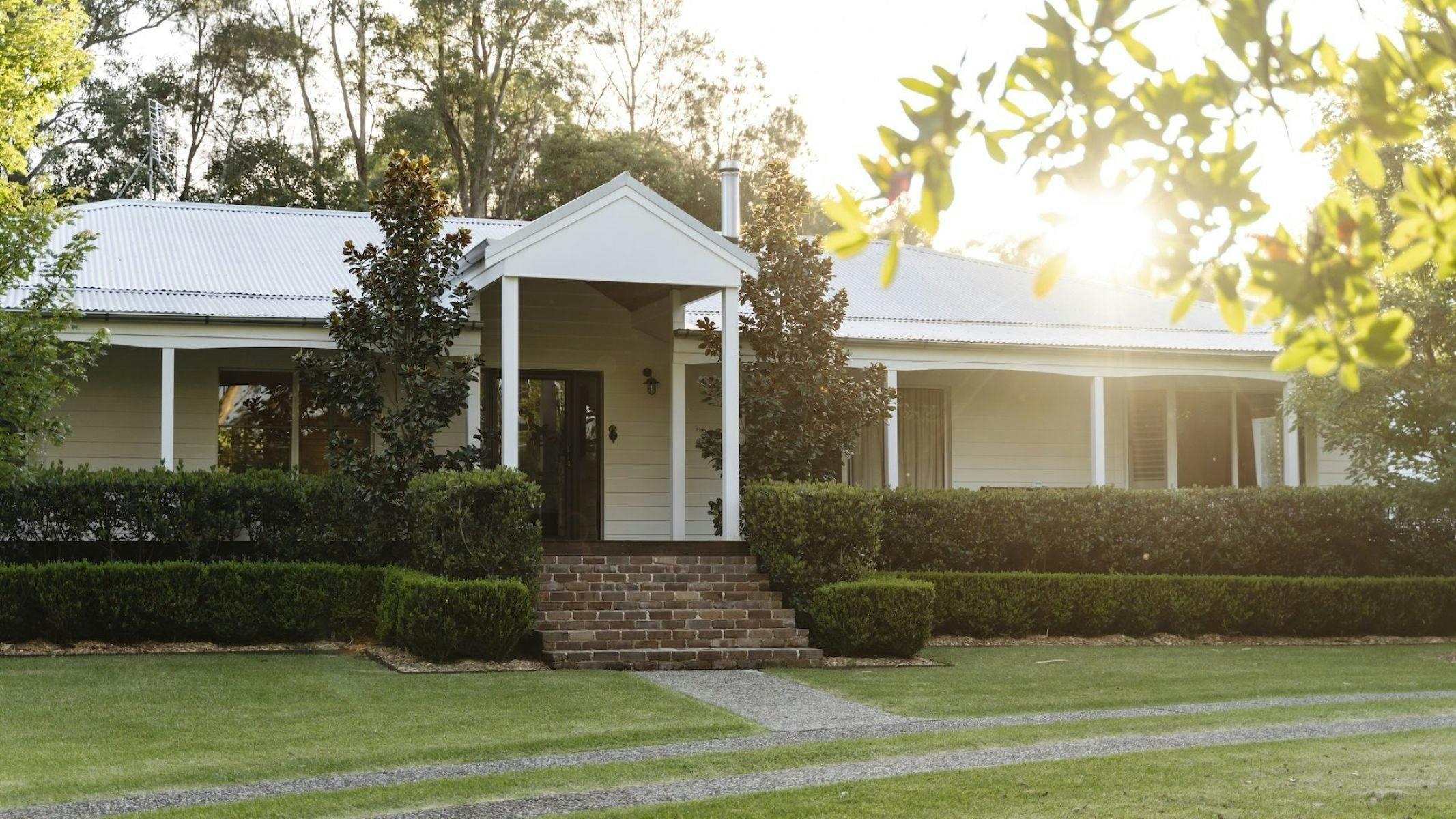 Image of front of house facade. Sun is going down behind property showing beautiful light