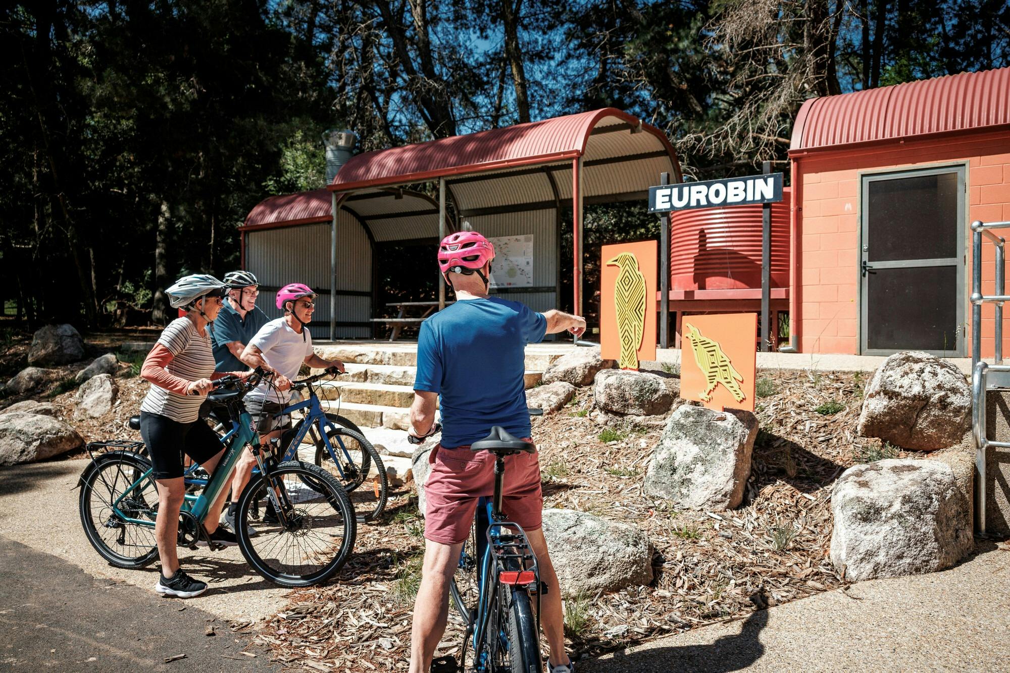 A group of cyclists look at indigenous artworks of native animals, infront of a sign saying Eurobin