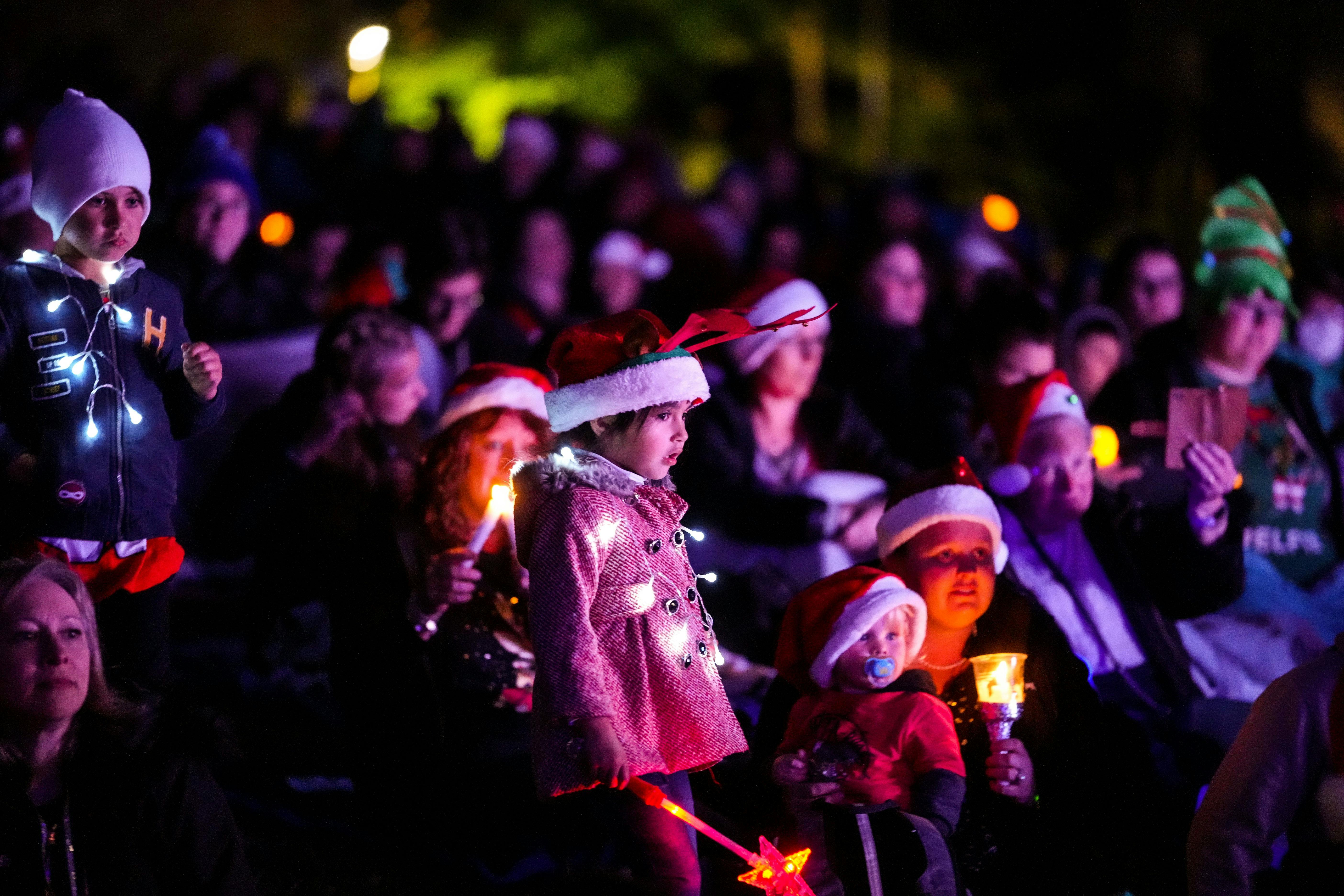 small girl in a pink coat with fairy lights, santa hat and candle in hand