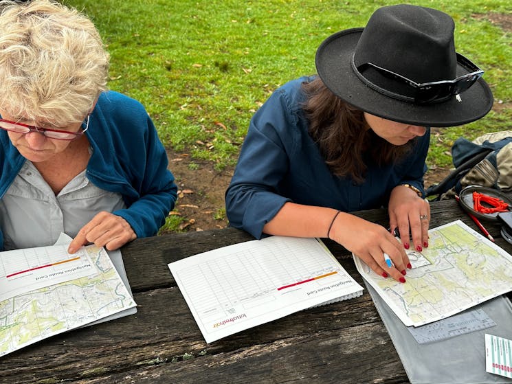2 women at outdoor table using maps and compass