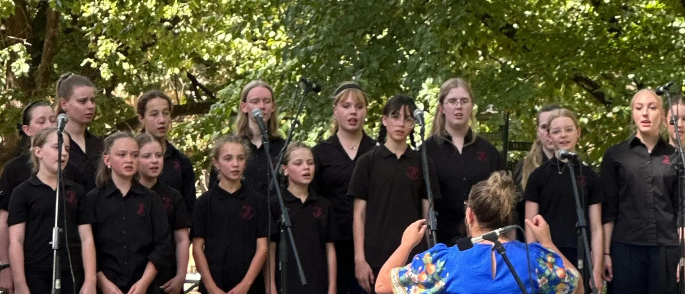 A choir of young people standing outside in front of microphones
