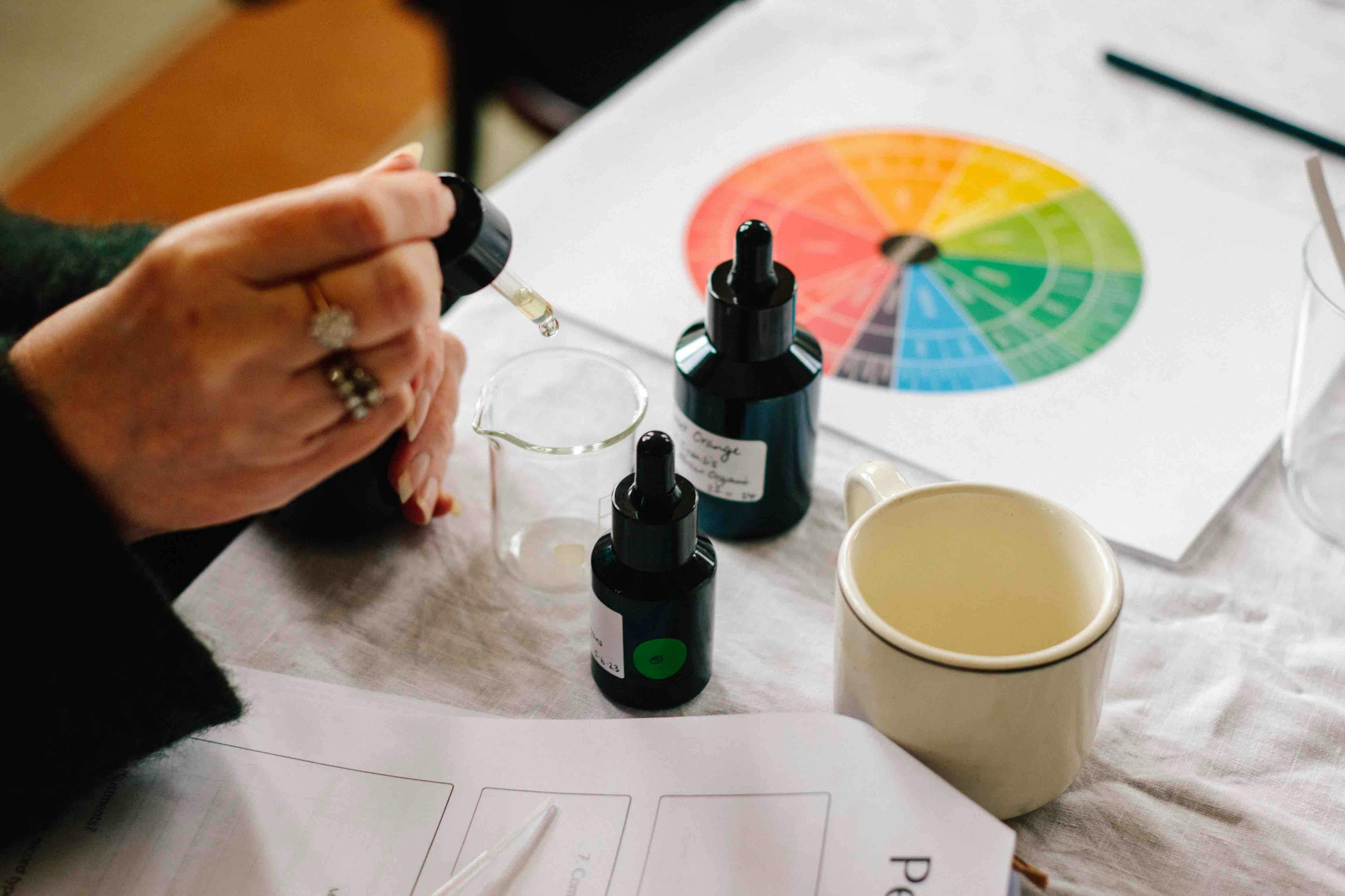 A hand drops oil into a beaker to blend perfume