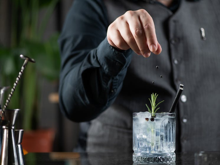 Bartender garnishing a gin and tonic with dried juniper berries