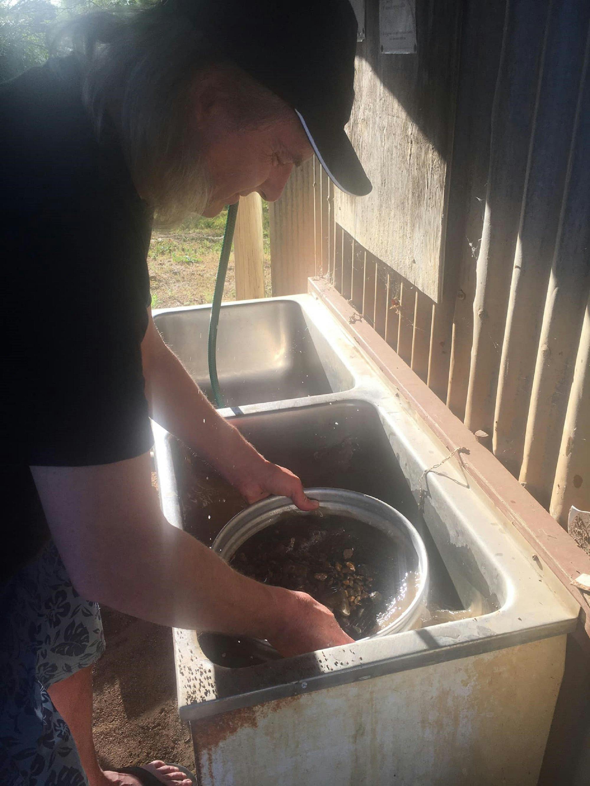 Man holding fossicking sieves in his hands over a tub of water