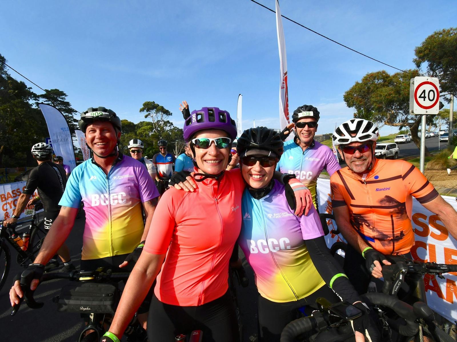 5 cyclists in bright jerseys smile at the camera before they start