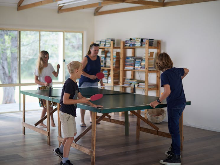 An adult and 3 children play table tennis inside the games room