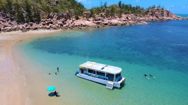 Aquascene boat in clear blue shallow water near beach edge with people swimming and sitting on beach Aquascene boat in clear blue shallow water near beach edge with people swimming and sitting on beach