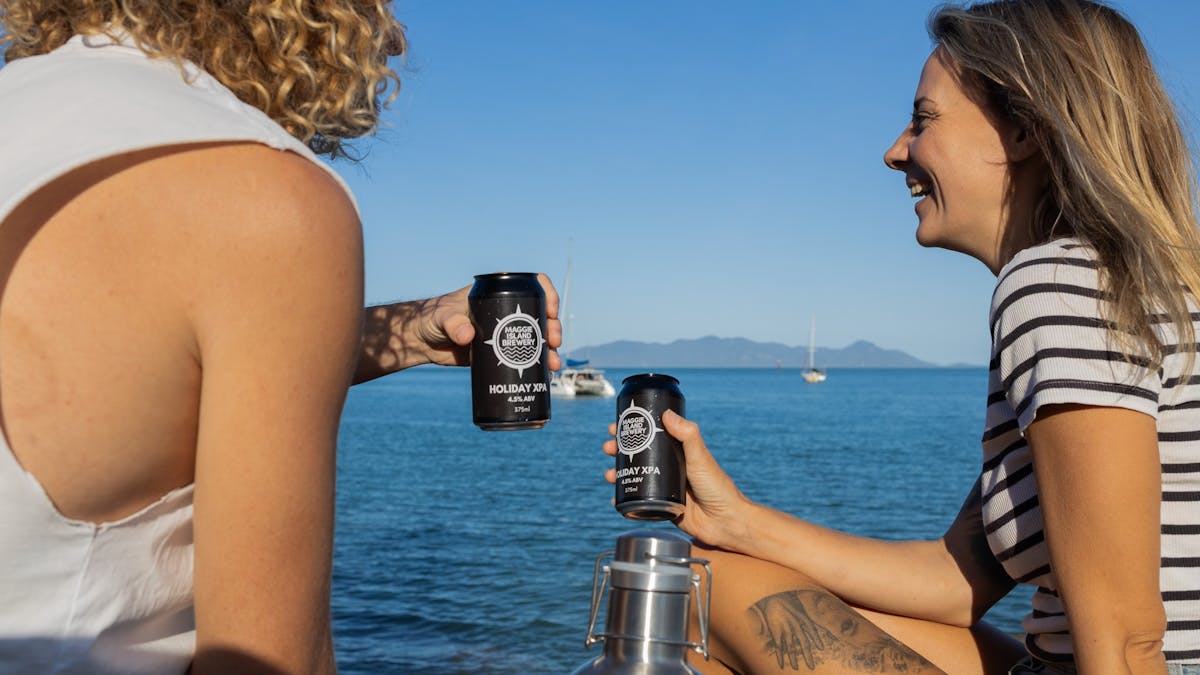 Two people toasting with takeaway beers while sitting on a rock