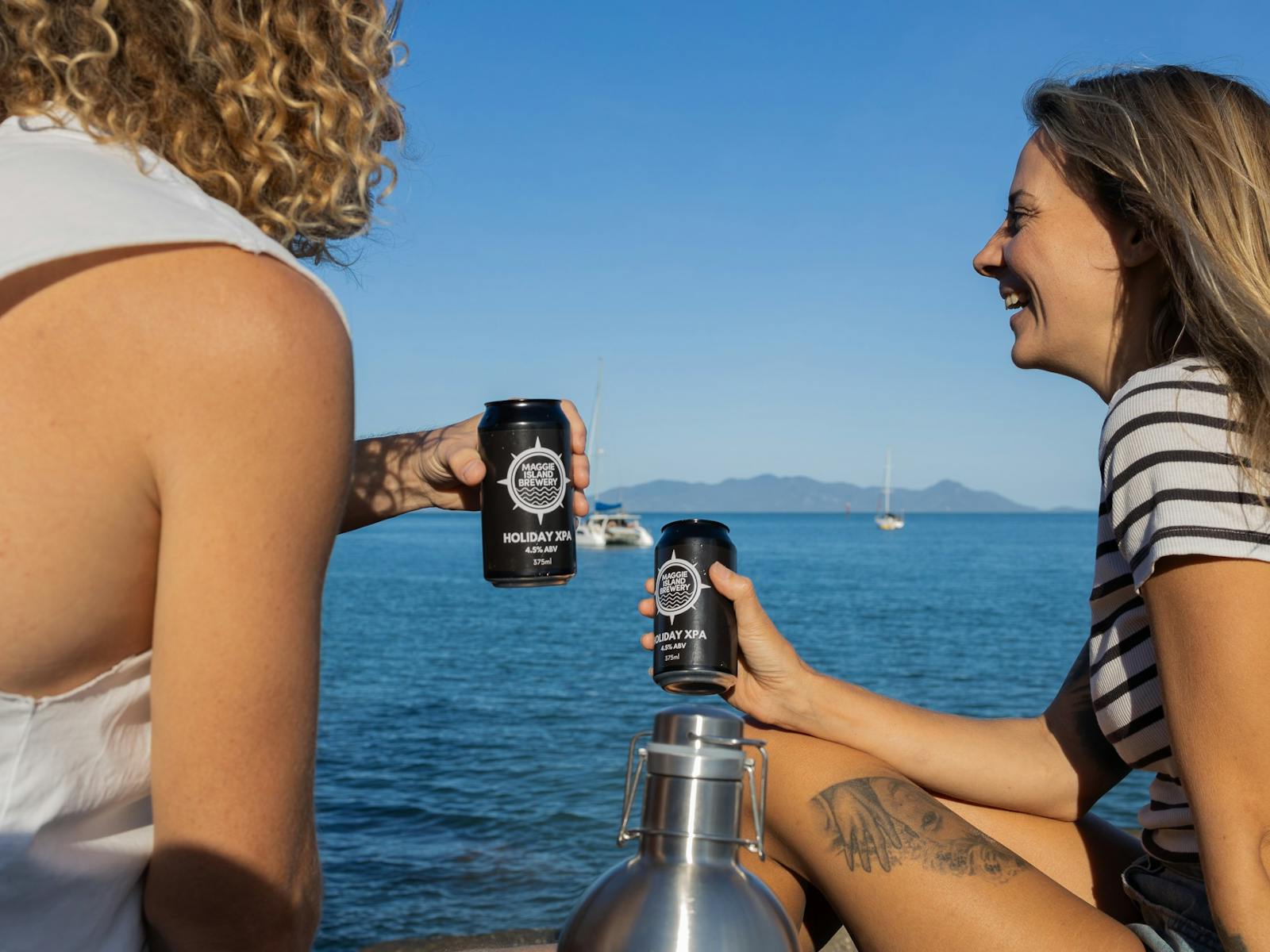 Two people toasting with takeaway beers while sitting on a rock Two people toasting with takeaway beers while sitting on a rock