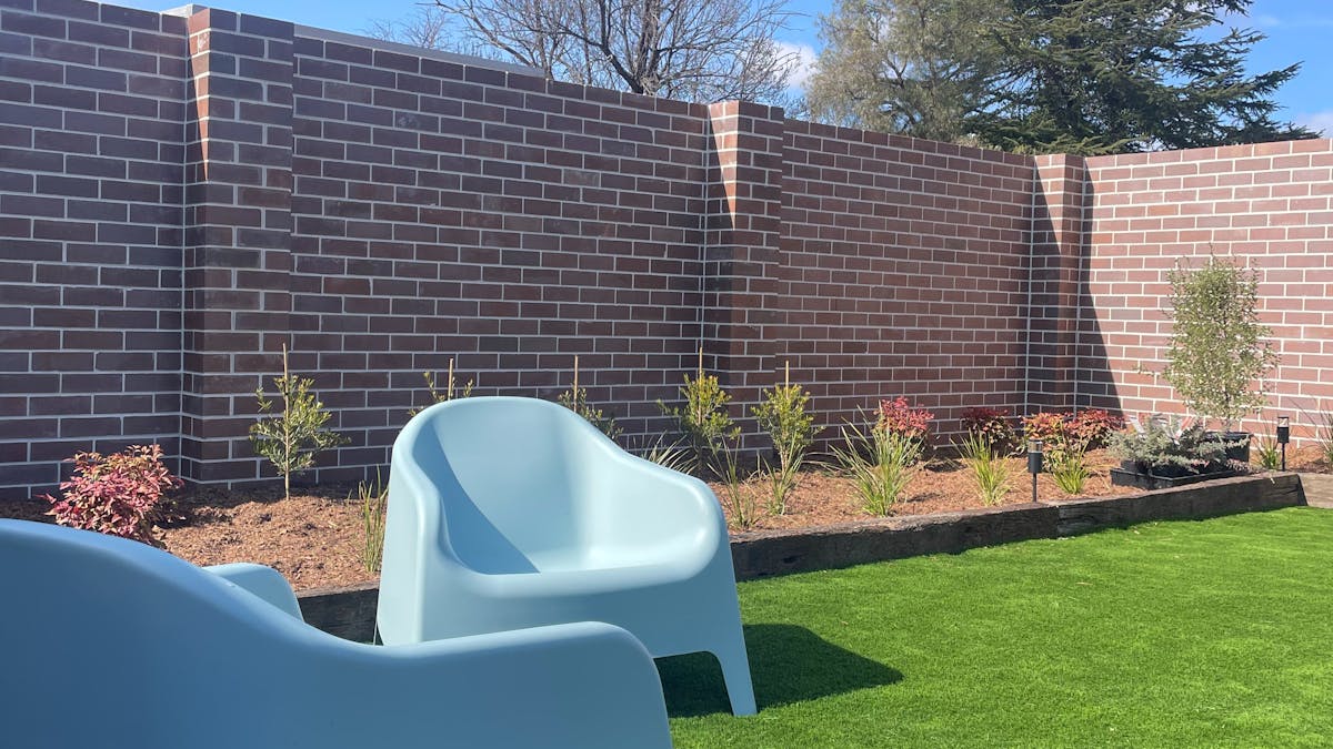 Gorgeous garden with artificial turf, red brick fence and modern blue garden lounge chairs.