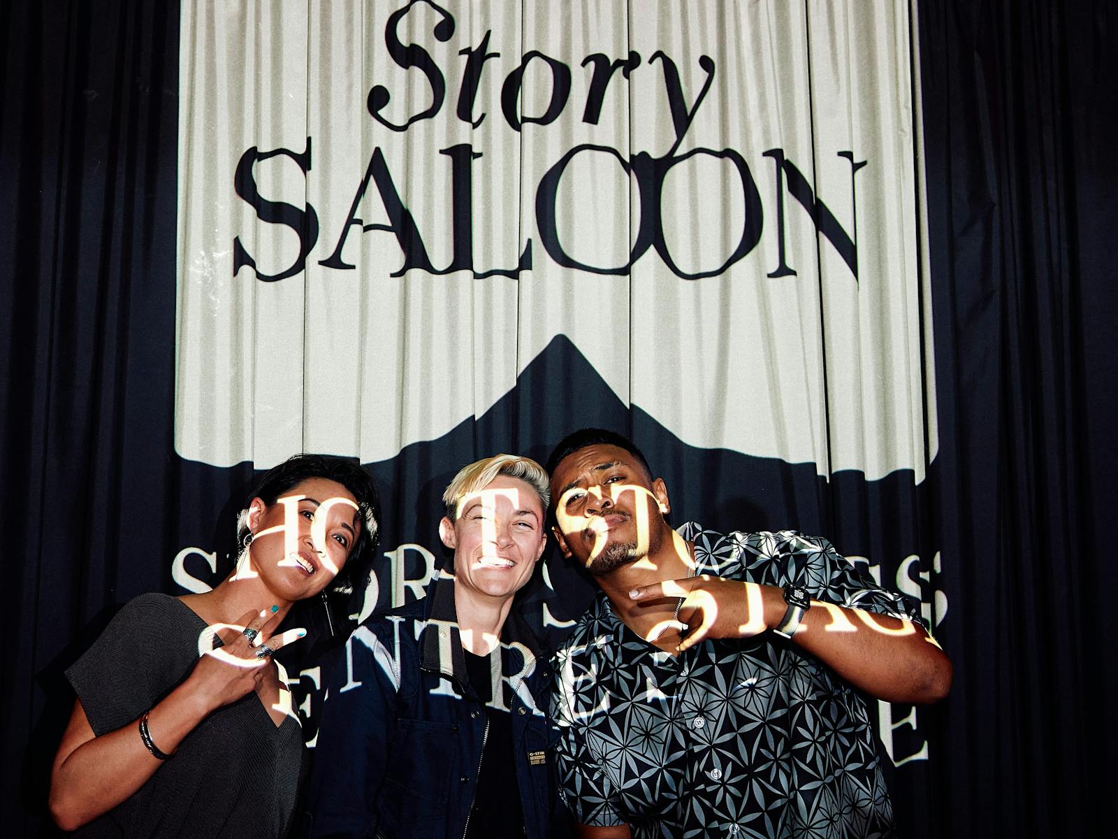 Three actors in front of a curtain with StorySALOON projected on to them