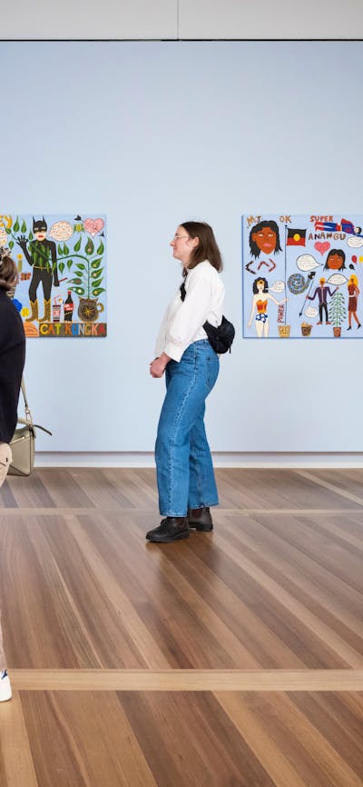 Three people look at colourful portraits hanging on pale blue walls. One of them holds a baby.
