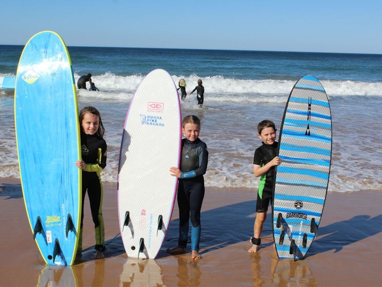 Three kids standing on the beach with surfboards.