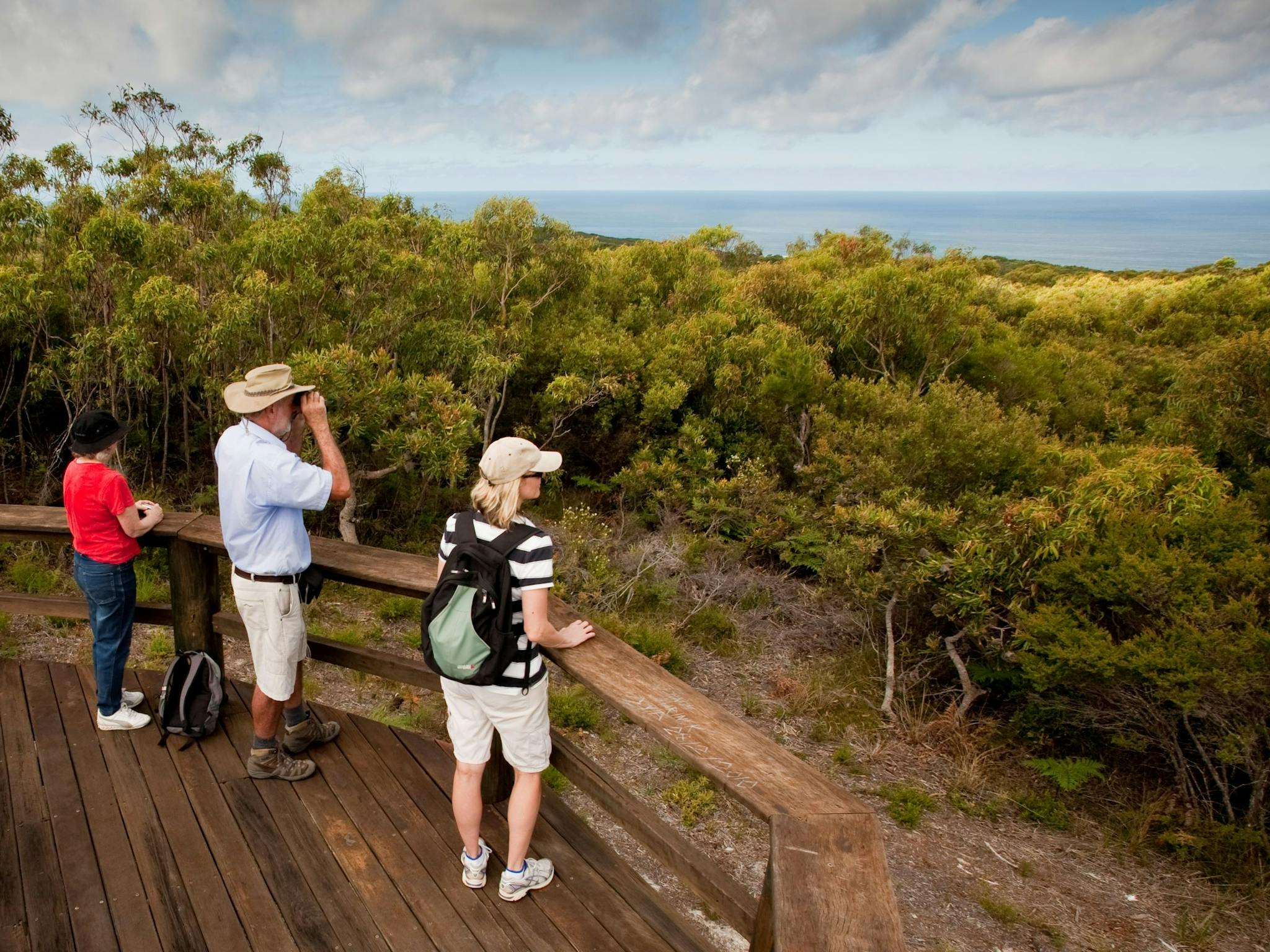 Three people at a wooden lookout. Three people at a wooden lookout.