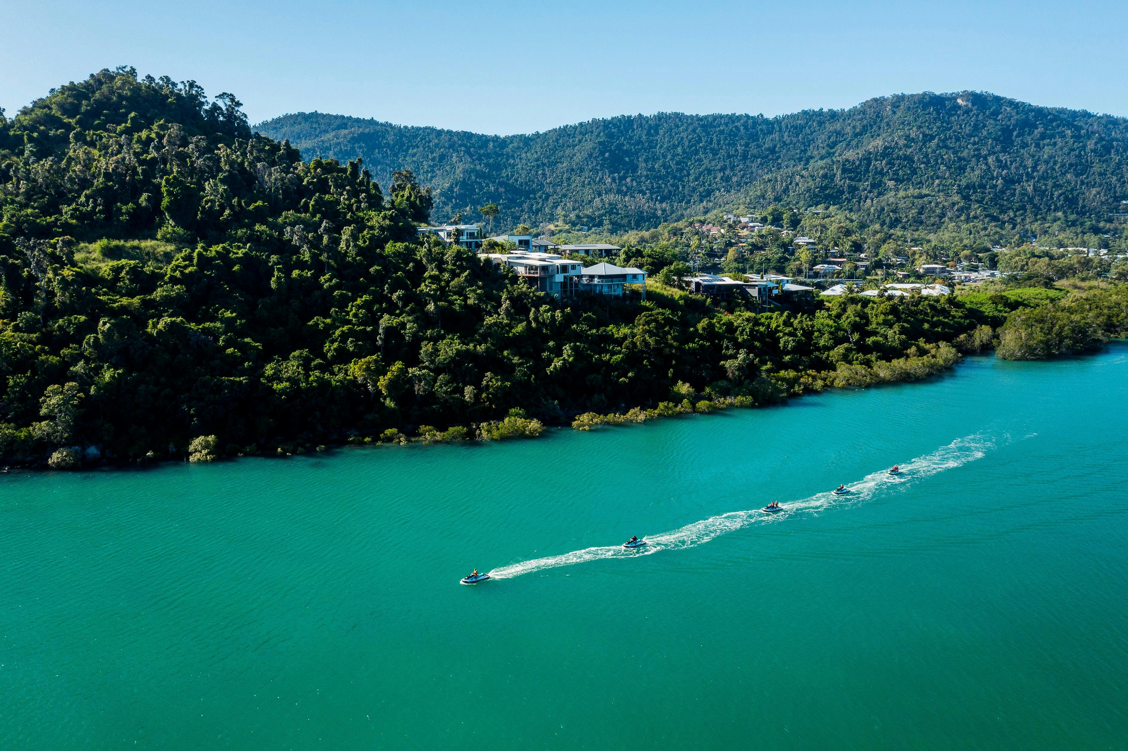 Jet skis driving along the bay in Cannonvale with private homes and hills in the background