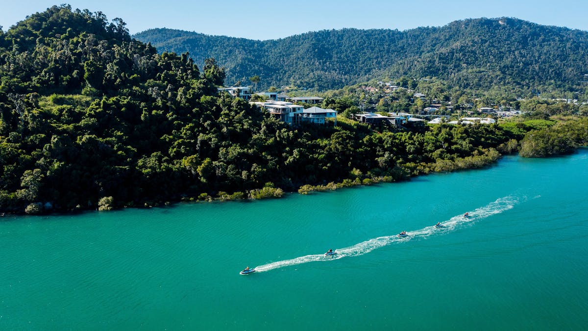 Jet skis driving along the bay in Cannonvale with private homes and hills in the background