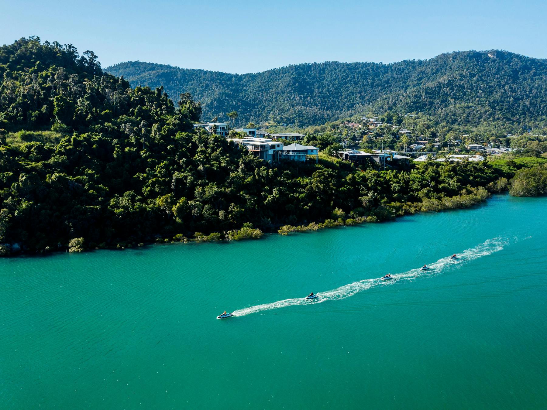 Jet skis driving along the bay in Cannonvale with private homes and hills in the background