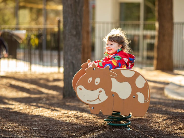 A young child playing on playground equipment shaped as a cow